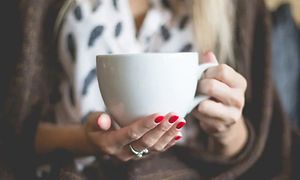 Närbild på en kvinna med röda naglar som håller i en stor vit kaffekopp. 