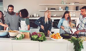 Sex personer som lagar mat tillsammans i ett stort kök. 