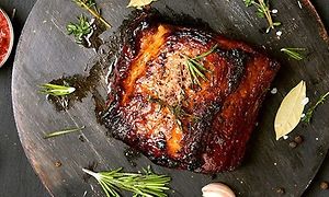 Stekt kött på en rund träskärbräda med kryddor, lime och viktlök strött runt omkring. Vid sidan står en liten skål med röd sås.