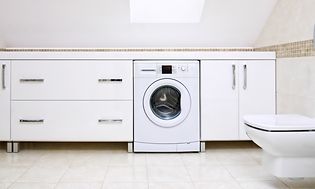 Integrerad tvättmaskin i ett stort vitt badrum med snett tak.
