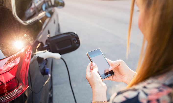 Kvinna som håller telefonen och laddar bilen