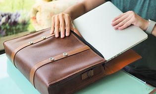 Person stoppar ner en bärbar dator i en brun portfölj eller väska. 