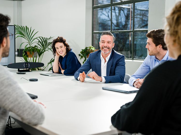 Personer runt ett bord i ett konferensrum på kontor med IRIS videokonferenssystem uppkopplat.