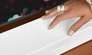 En hand som trycker på en vit sonos beam 2 soundbar.