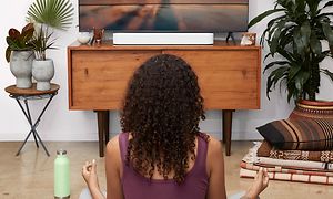 Kvinna som sitter i lotusställning framför en TV med en vit soundbar under.