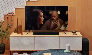 Tv med soundbar placerad på en TV-bänk, kvinna med ett glas vin syns på skärmen.