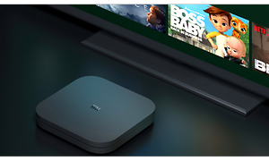 En svart Xiaomi mi TV-box framför en TV med olika små bilder på.