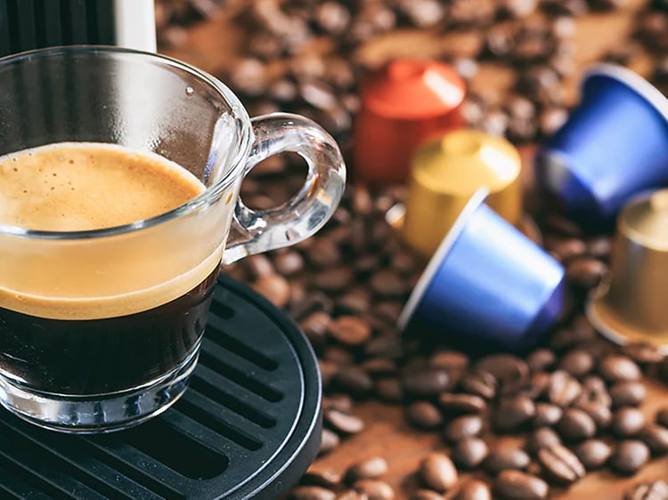 En kopp espresso från en kapselmaskin och  kapslar och kaffebönor på bordet