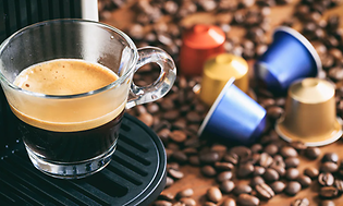 En kopp espresso från en kapselmaskin och kapslar och kaffebönor på bordet