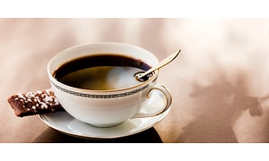 En kopp med svart kaffe och en kaka vid sidan på kaffefatet. 