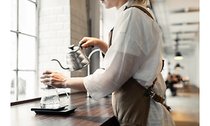 En kvinna häller upp varmt vatten i ett filter över en kanna, så kallat "pour over"-kaffe.