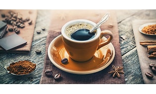 En kopp espresso med fat och kaffebönor runt omkring.