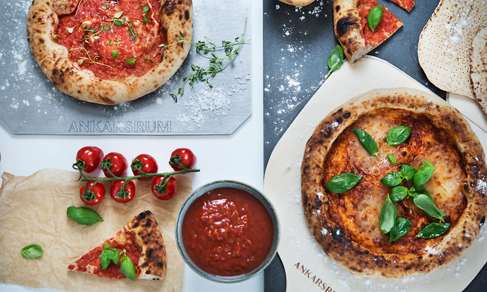 Ankarsrum Pizzastål med två olika små pizzor och tomatsås vid sidan av.