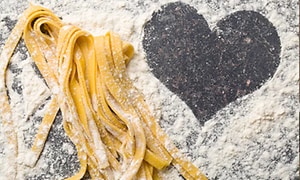 Hemlagad pasta på ett bord med mjöl och ett hjärta format i mjölet. 