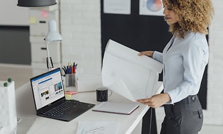 Kvinnlig arkitekt ser på en ritning med Lenovo ThinkPad bredvid sig på ett bord. 