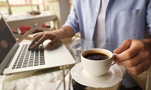 En person som jobbar på en bärbar dator med en kopp kaffe bredvid. 