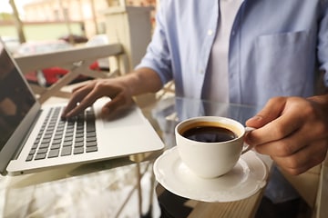 En person som jobbar på en bärbar dator med en kopp kaffe bredvid. 
