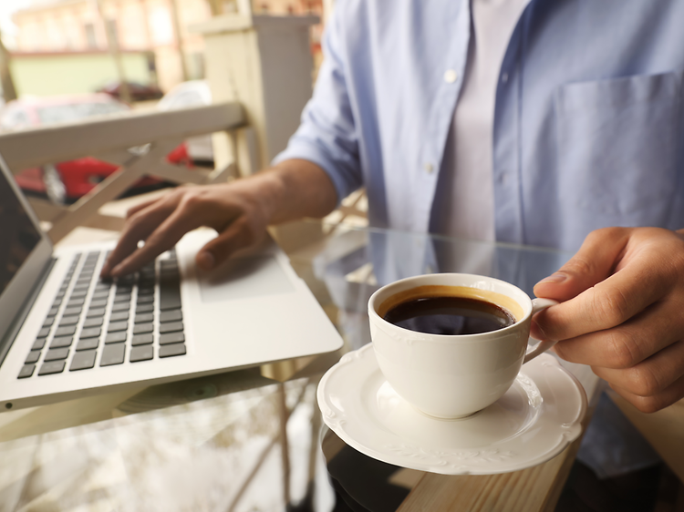 En person som jobbar på en bärbar dator med en kopp kaffe bredvid.