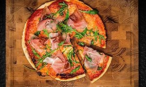 Pizza med skinka och ruccola på en träskärbräda med en slice utskuren.