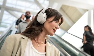 Kvinna som är på väg ner i en rulltrappa med vita Bose hörlurar på sig.