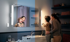 Philips Hue Adore downlights i badrum där ett barn står med en vuxen och borstar tänderna. Ena sidan är blå och andra orange. 