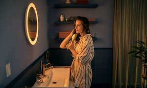 Kvinna borstar håret framför en Philips Hue Adore mirror med ljus runt. 