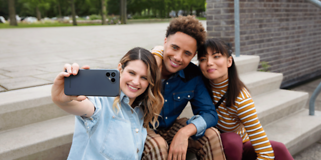 Fairphone 4 i handen på en kvinna som tar en selfie med två andra