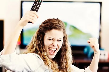 jublande kvinna framför en TV med en fjärrkontroll i handen