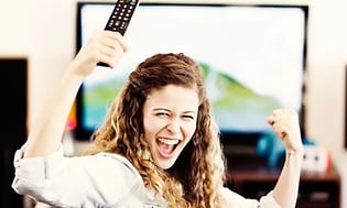 jublande kvinna framför en TV med en fjärrkontroll i handen