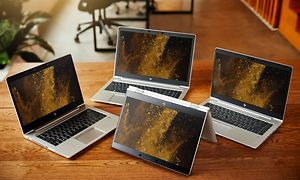 Fyra HP EliteBook bärbara datorer på ett träbord.