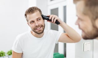 En man klipper sitt hår med en hårtrimmer.