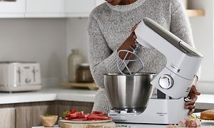 Kvinna lyfter köksmaskinens huvud där ett K-beater-verktyg är fäst