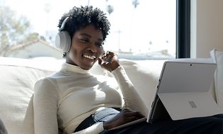 Kvinna ler mot Surface Pro medan hon har på sig hörlurar