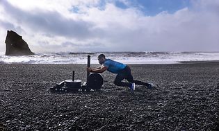 Garmin Fenix 6 på handleden på en man som tränar med vikter på en stenig strand