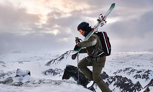 Garmin Fenix 6 på handleden på en man som bär sina skidor och går uppför ett berg med snö