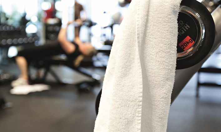 En vit handduk hänger i ett gym med personer som tränar i bakgrunden