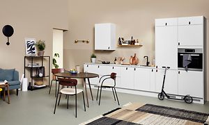 Ett vitt EPOQ Core kök med öppen planlösning, soffa och ett runt matbord i mitten. En sparkcykel står också i köket. 