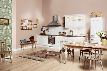 Vitt EPOQ Heritage kök med öppen kökslösning och rosa väggar. Köksbord i trä och vivaror från smeg. 