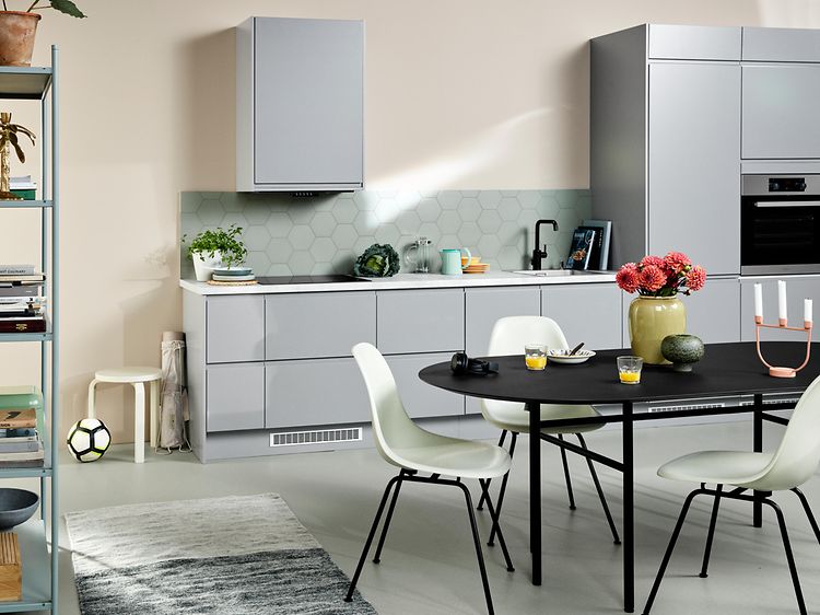 Ljusgrått EPOQ Integra kök med öppen kökslösning, ett svart köksbord med vita stolar och en bokhylla. 