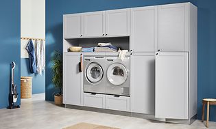 Ljusgrå tvättstuga från EPOQ Shaker med blå väggar, tvättmaskin och torktumlare integrerat och en skaftdamsugare vid väggen. 