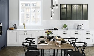 Vitt kök från Epoq Shaker med ett stort avlångt köksbord med svarta stolar. Glasskåp upphängt på ena väggen. 