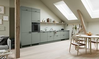 EPOQ Trend kök i färgen sage med öppen planlösning, integrerad ugn och spishäll, runt köksbord med stolar i ljus träfärg.