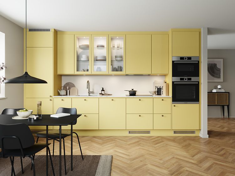 EPOQ Trend kök i påskgul färg som kallas Mellow med öppen planlösning, integrerad ugn, glasskåp och svart köksbord.