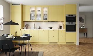 EPOQ Trend kök i påskgul färg som kallas Mellow med öppen planlösning, integrerad ugn, glasskåp och svart köksbord.