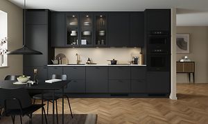 Svart kök med öppen planlösning och integrerad ugn, glasskåp och ett svart köksbord med stolar och lampa i samma färg.