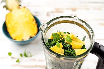 Halv ananas bredvid en blender med spenat och ananas