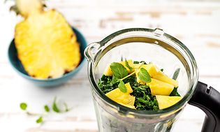 Halv ananas bredvid en blender med spenat och ananas