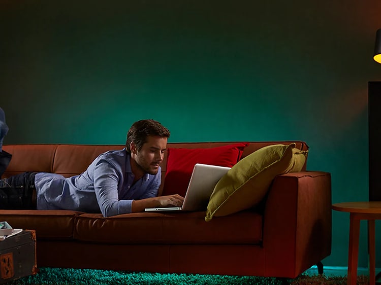 Man ligger på soffa och använder bärbar dator med olika smartlampor runt sig