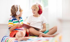 Hörlurar för barn - Två barn lyssnar på något i sina hörlurar och ler till varandra.