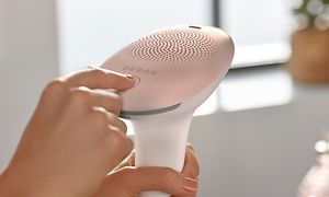 En hand som trycker på en knapp på Philips IPL-hårborttagningsenhet